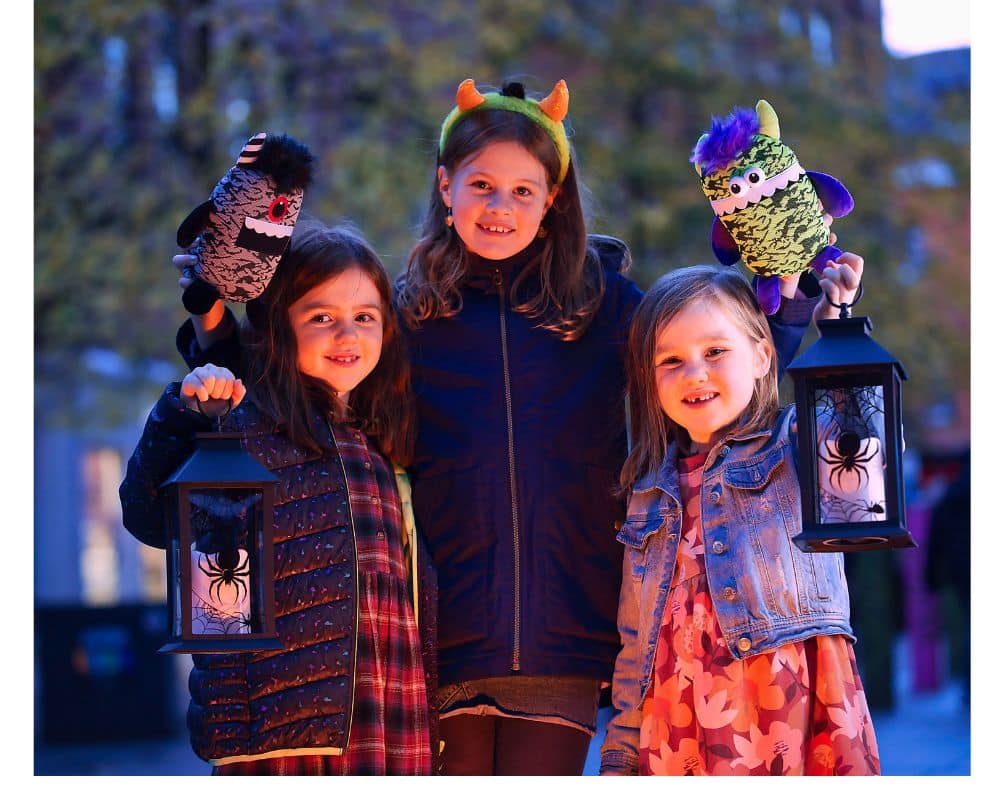 Three children with lanterns, Halloween toys and big smiles . All three are little girls. 