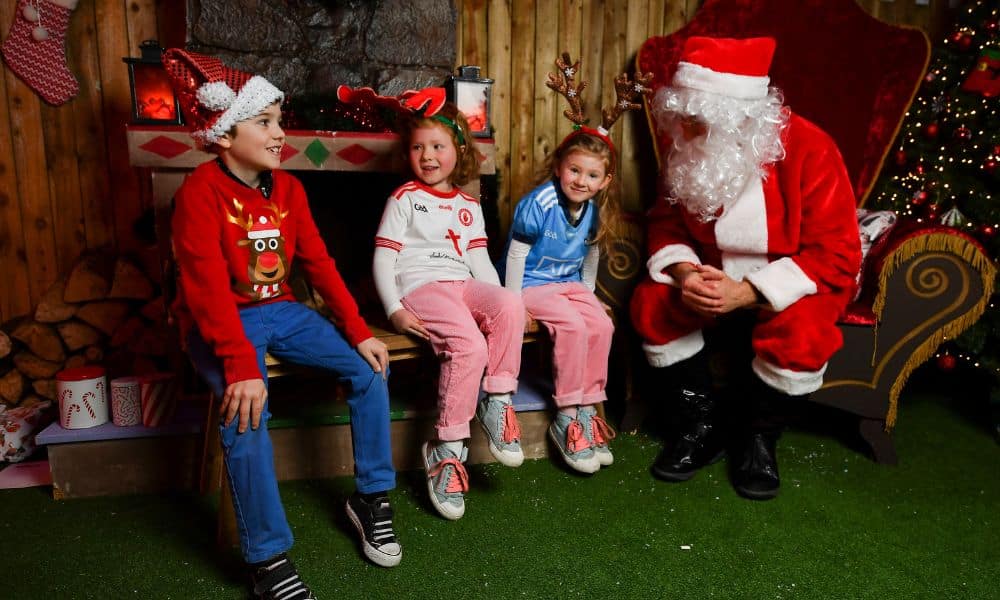 Three children in Christmas special outfits sit on the side of Santa Claus and they look happy - this Santa Experience photograph is from Croke Park