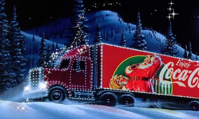 A bright red truck - the Coca-Cola truck and the background is snowy, with trees and a white Christmas feel