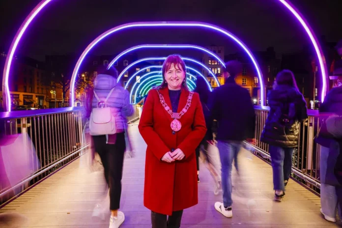 The Lord Mayor of Dublin stands in front of winter lights that are switched on - rings and arches