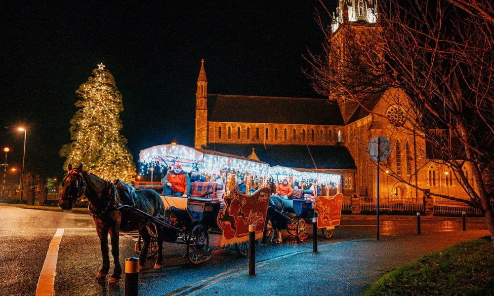 A horse drawn carriage with Christmas lights and decorations in Killarney. At the backdrop is a church/cathedral. These sleighs can be booked for the Christmas experience. 