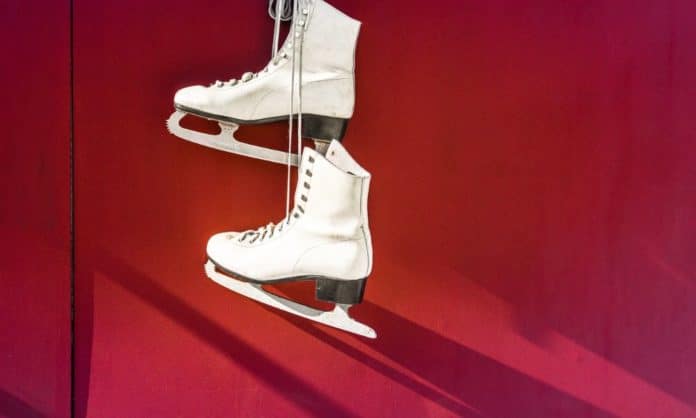 A pair of white ice-skating boots against a red background