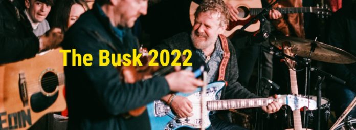 Musicians playing at The Busk with text in yellow saying The Busk 2022