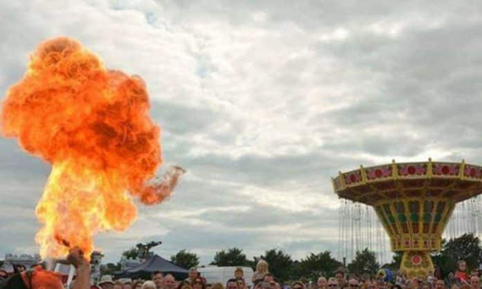 You see a performer having a fire eating show and children and families at the fun fair