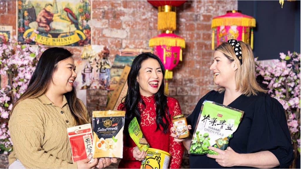Three women (panellists) holding food packets and products for the Flash in the Pan panel discussion - a representative pic for the discussion that will take place for Chinese Lunar Year Celebrations