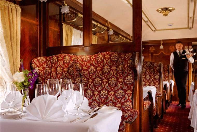 An inside view of the Pullman Restaurant with a waiter with drinks in hand and lush surroundings looking like a luxury train carriage