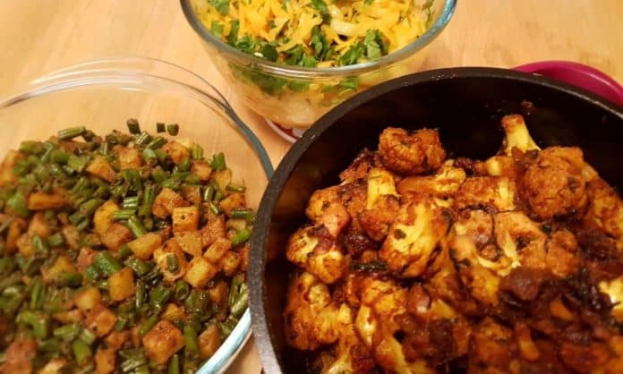 Three containers - one has a potato and cauliflower floret curry, another has beans and potatoes, and third is also a vegan dish - cabbage fry