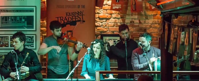 Musicians & singers with their instruments against a backdrop of Kilkenny TradFest