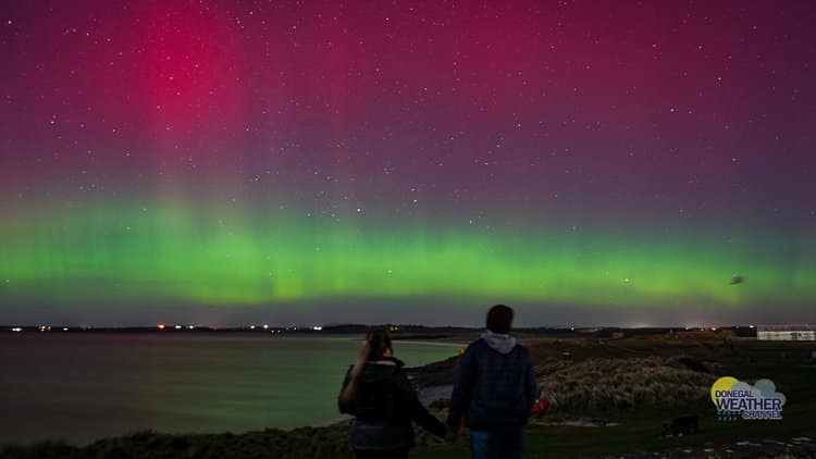 A couple watching Northern Lights in Donegal over the sea
