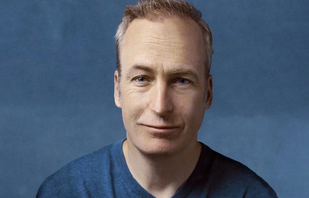 Bob Odenkirk wearing a navy blue T-shirt against a blue background as well