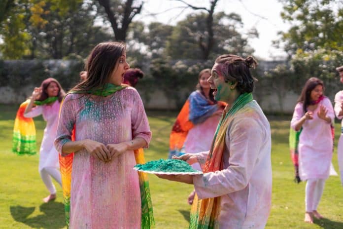 Women in white outfits hold plates of colours and celebrate Holi