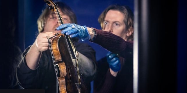 Two men on the Titanic Belfast experience examining a violin
