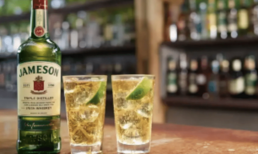 A Jameson whiskey with two glasses full of the drink and behind it is a bar at Jameson distillery tour