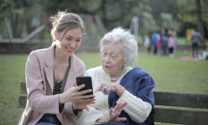 An adult woman and her elderly mother on a park bench sharing updates on Mother's Day